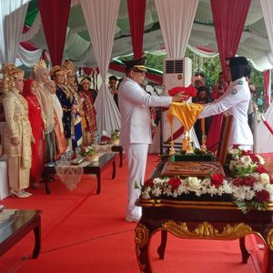 Bupati OKU H Teddy Meilwansyah SSTP MM MPd menyerahkan duplikat bendera pusaka kepada petugas pembawa baki untuk dikibarkan pada HUT RI ke 80 tahun 2025 di Taman Kota Baturaja. Kanalberita.id / Edo