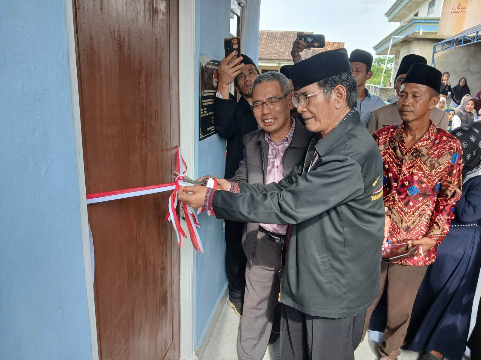 Ketua DPP PCTA Kanjeng Romo I Dewa Nyoman S Hartana didmapingi Sekdin PERKIM OKU Solihin SIP ST MT memotong pita di depan pintu masuk rumah syukur mensyukuri hari Pahlawan, Minggu (15/2/2026) sore. Kanalberita.id / Edo